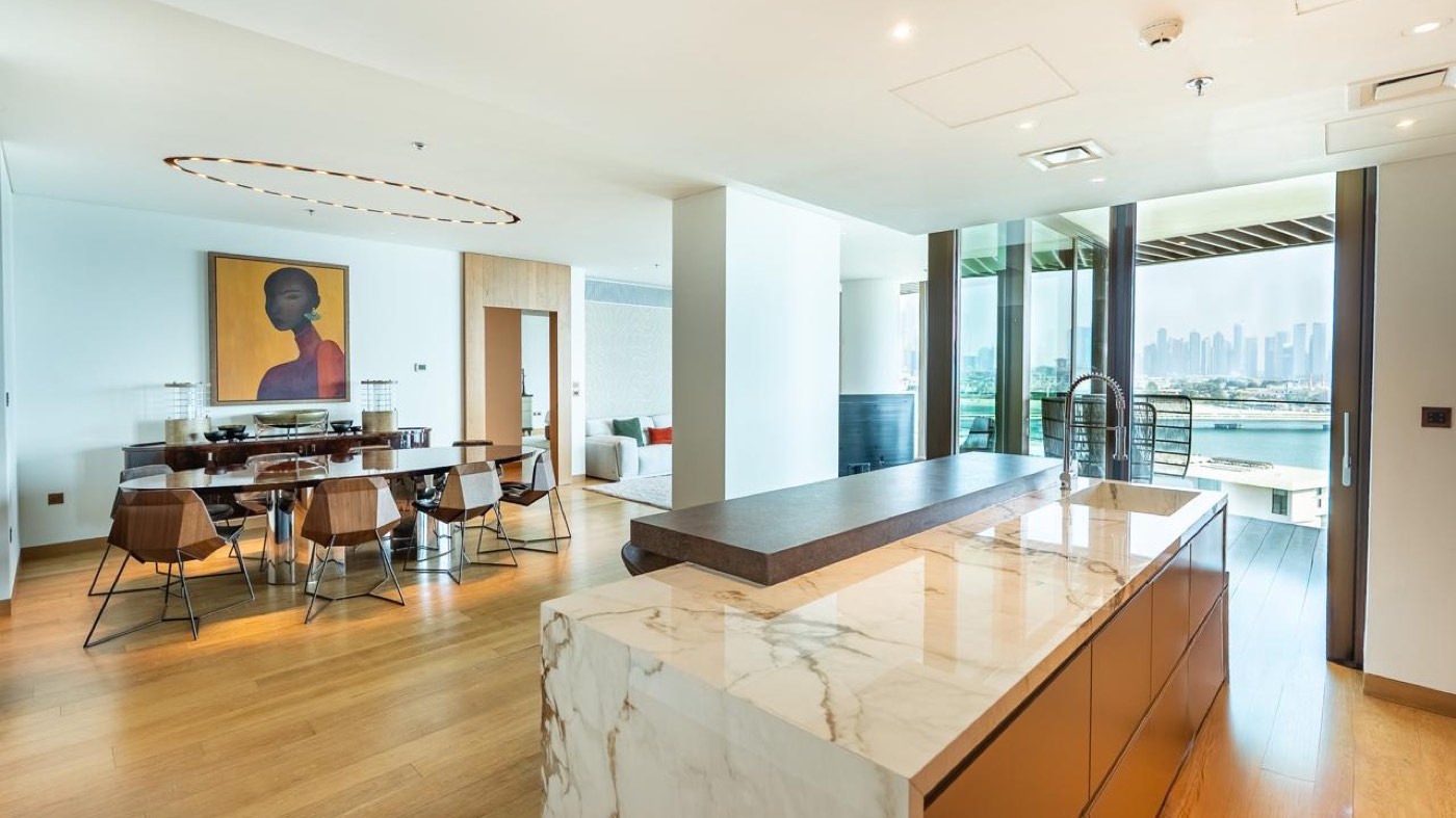 Open kitchen and dining room inside a Bvlgari Residences apartment on Jumeira Bay Island with a marble island, oak floors and floor to ceiling glass onto the Dubai skyline