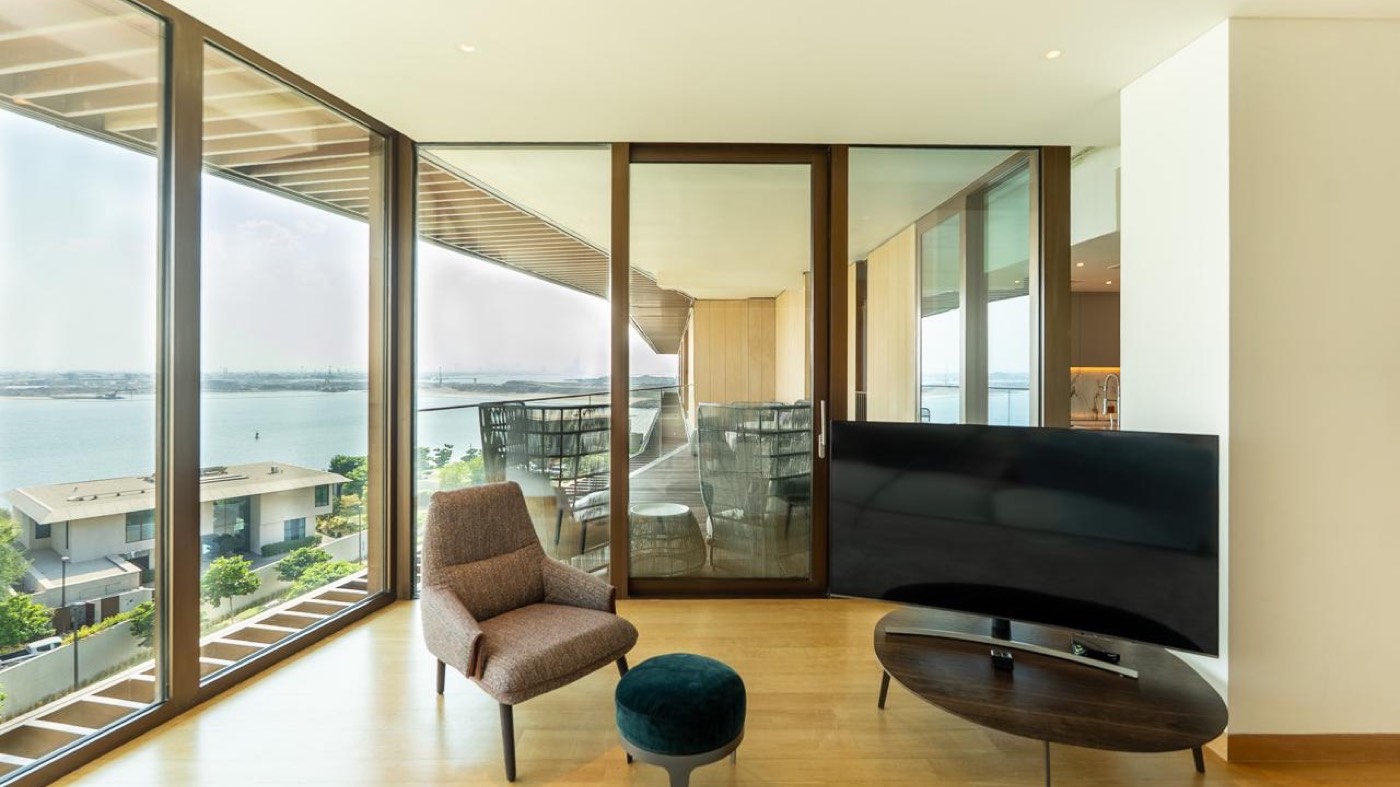 Living room of a Bvlgari Residences Dubai apartment with corner floor to ceiling glass, a wraparound terrace and views over the Jumeira Bay mansions and the Arabian Gulf