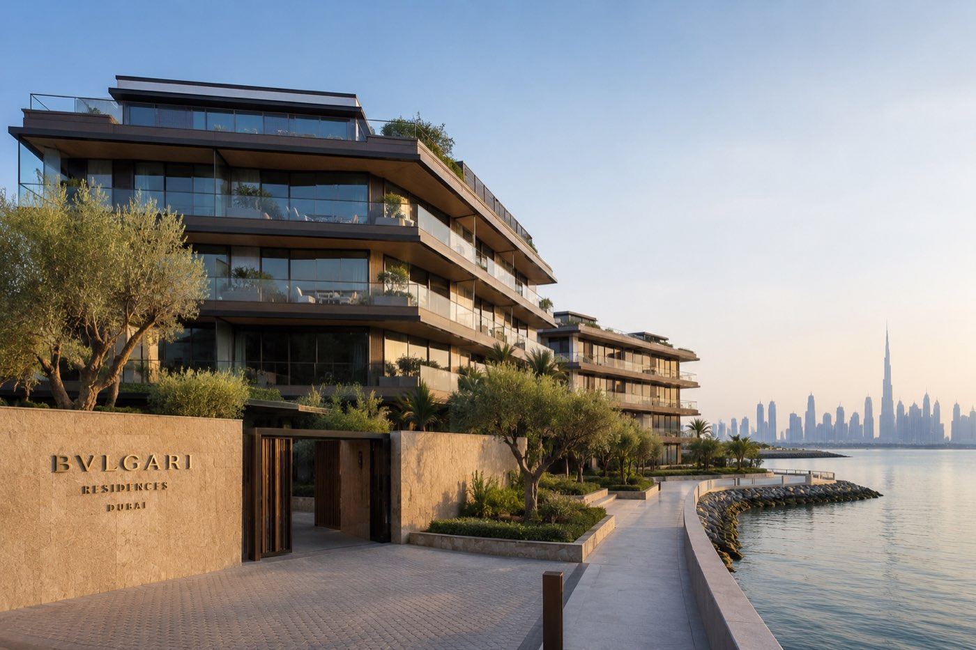 Bvlgari Residences Dubai entrance on Jumeira Bay Island at golden hour with stone signage, olive trees and the Downtown Dubai skyline across the water
